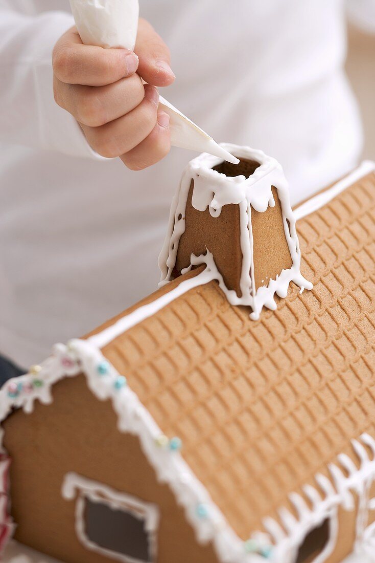Child decorating gingerbread house with piping bag