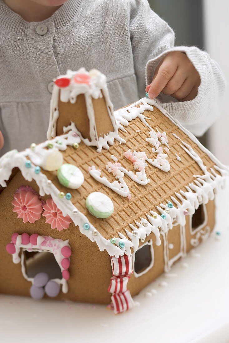 Child decorating gingerbread house with sugar pearls