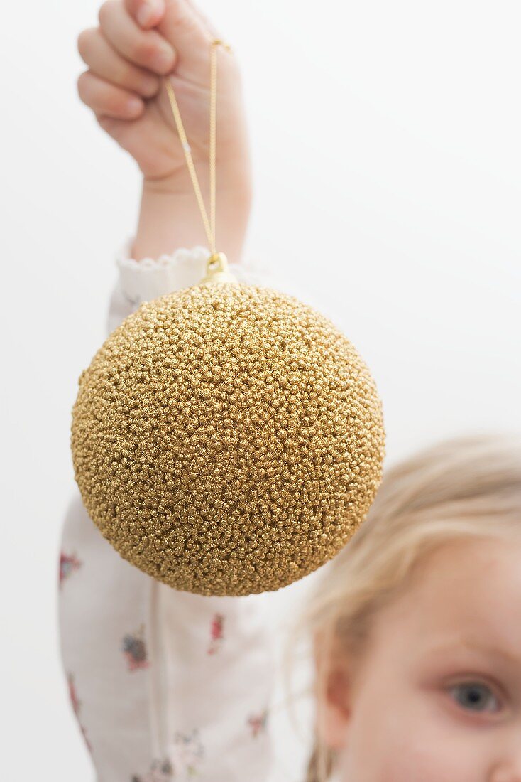 Kleines Mädchen hält goldene Christbaumkugel