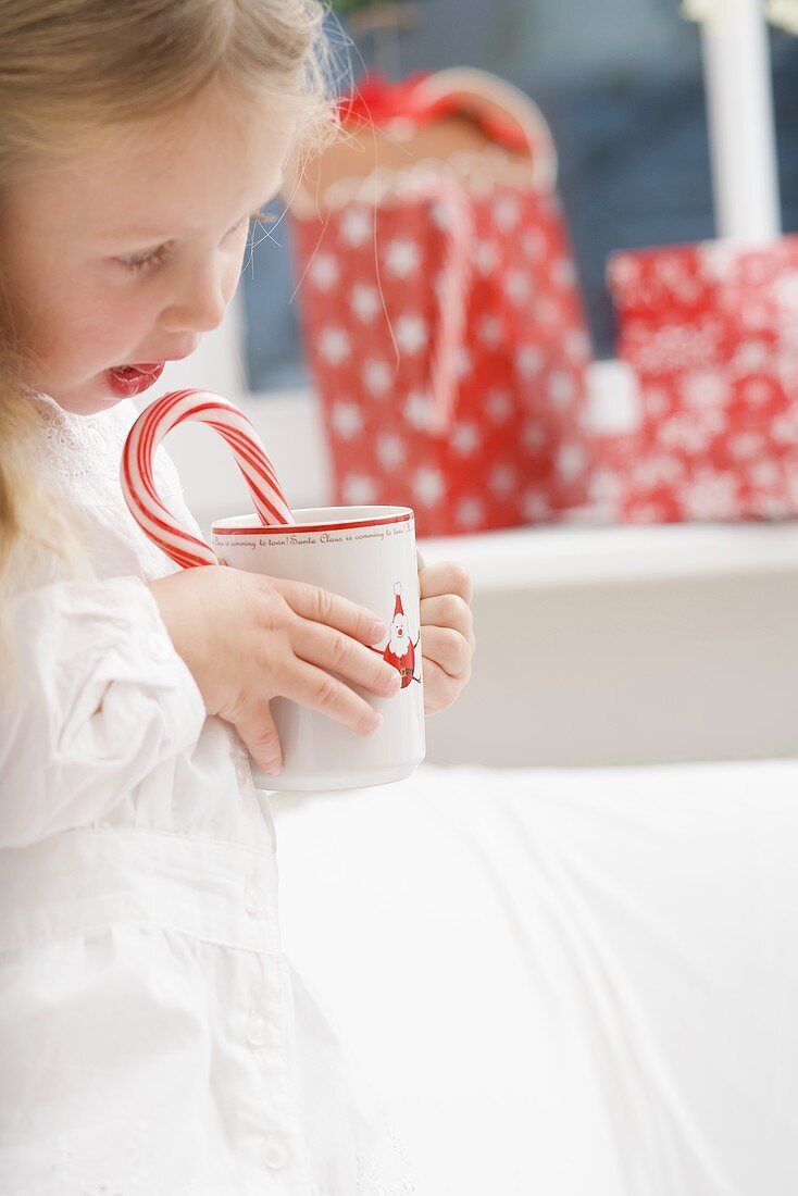 Small girl holding cup of cocoa with candy cane