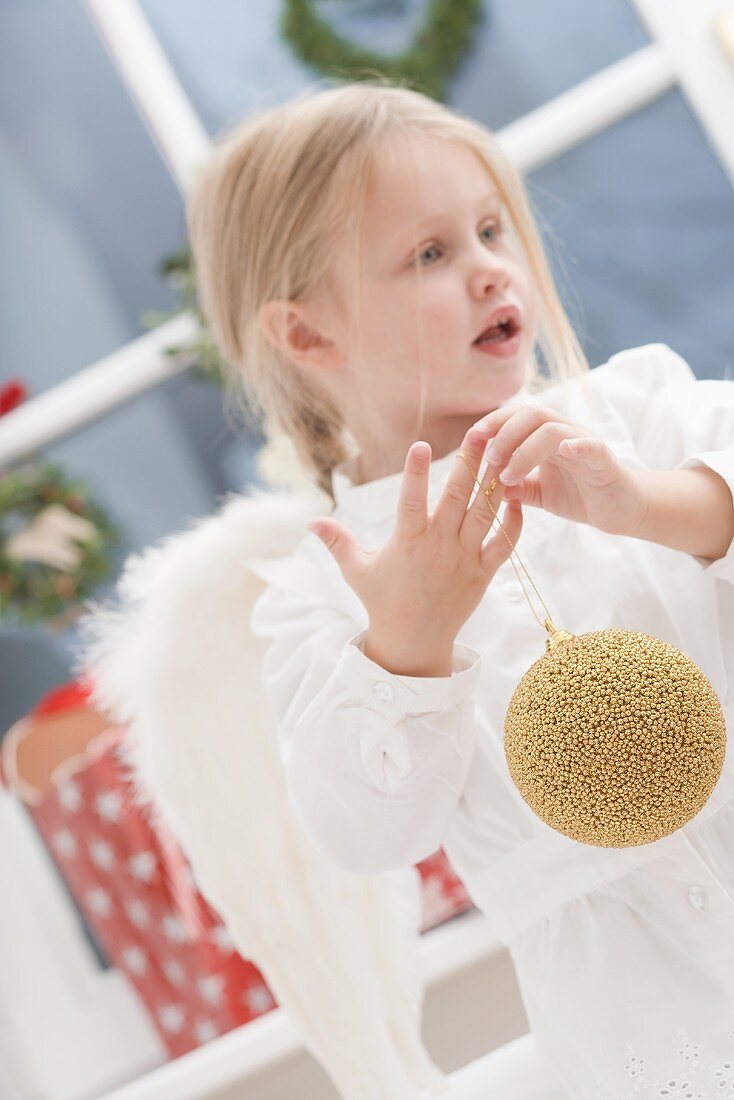 Kleines Mädchen mit Engelsflügeln und Christbaumkugel