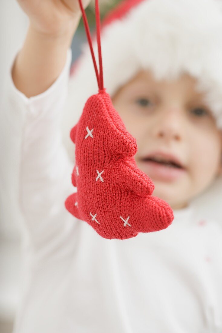 Child in Father Christmas hat holding Xmas tree ornament