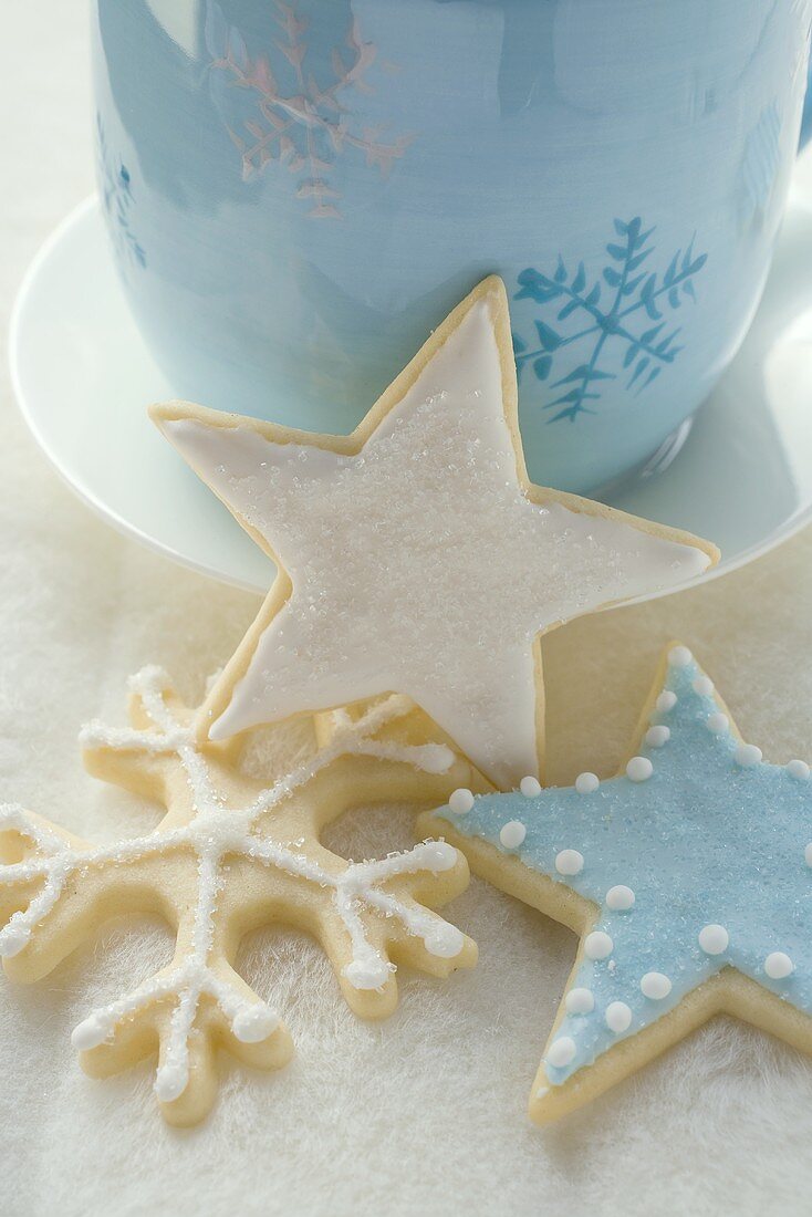 Three iced Christmas biscuits in front of blue cup