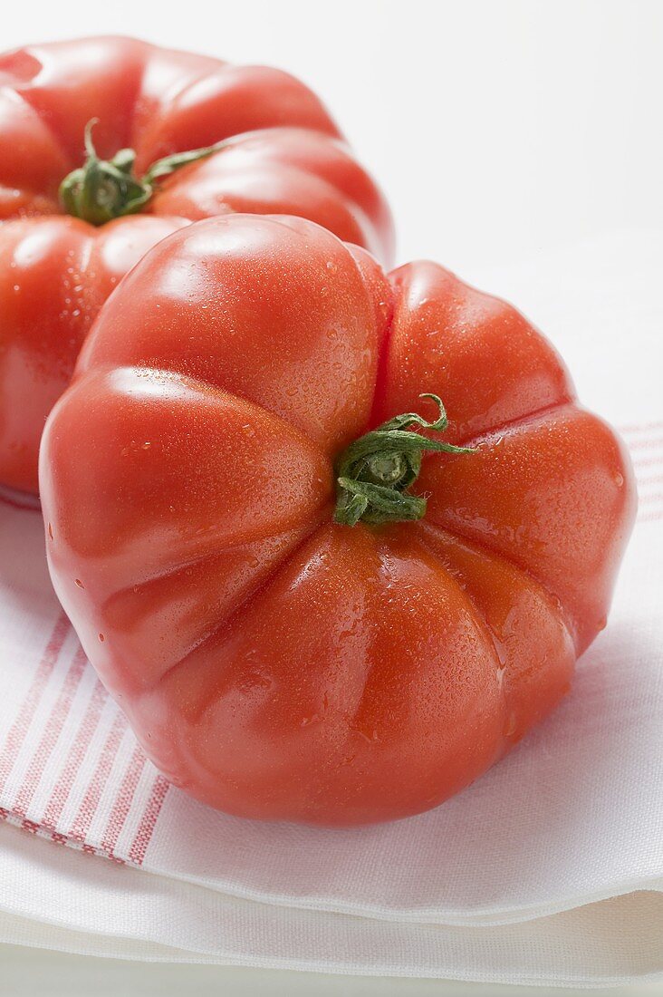 Two beefsteak tomatoes with drops of water on tea towel