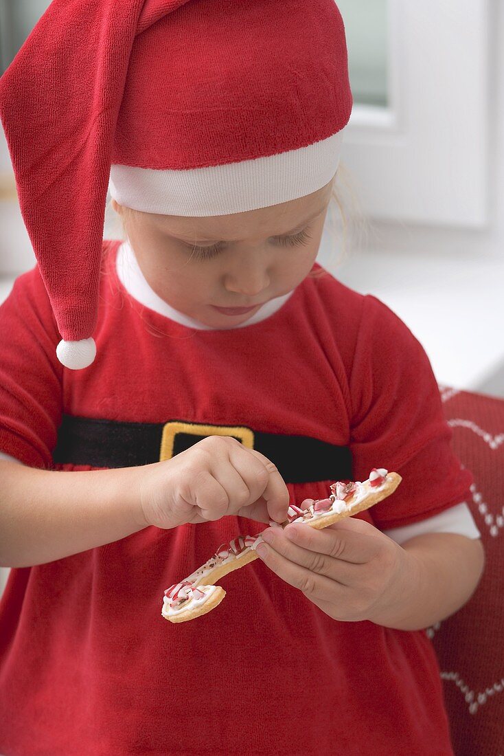 Kleines Mädchen im Weihnachtsmannkostüm verziert Plätzchen