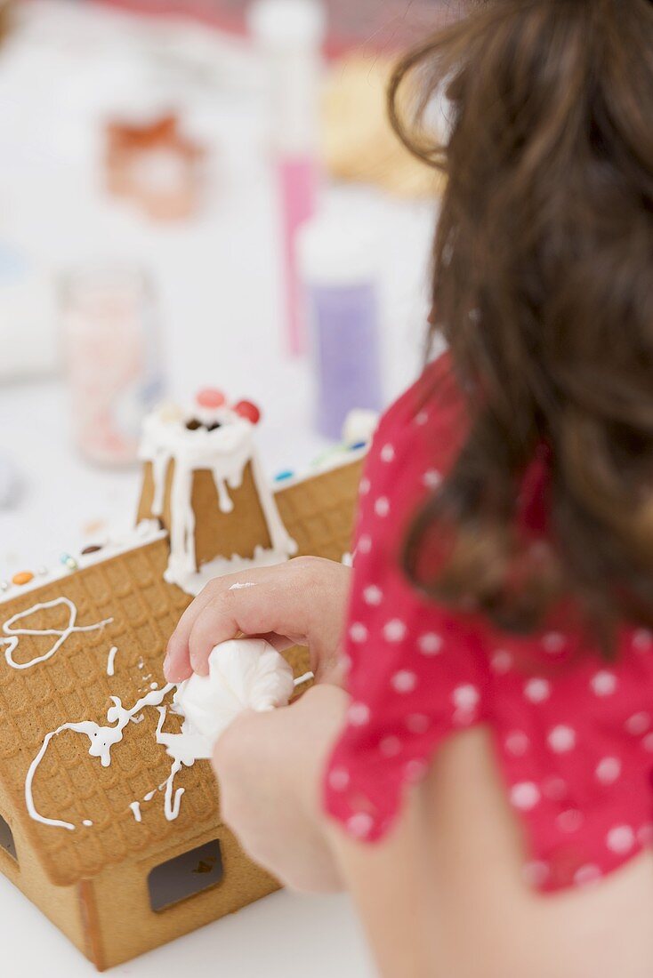 Small girl decorating gingerbread house using piping bag