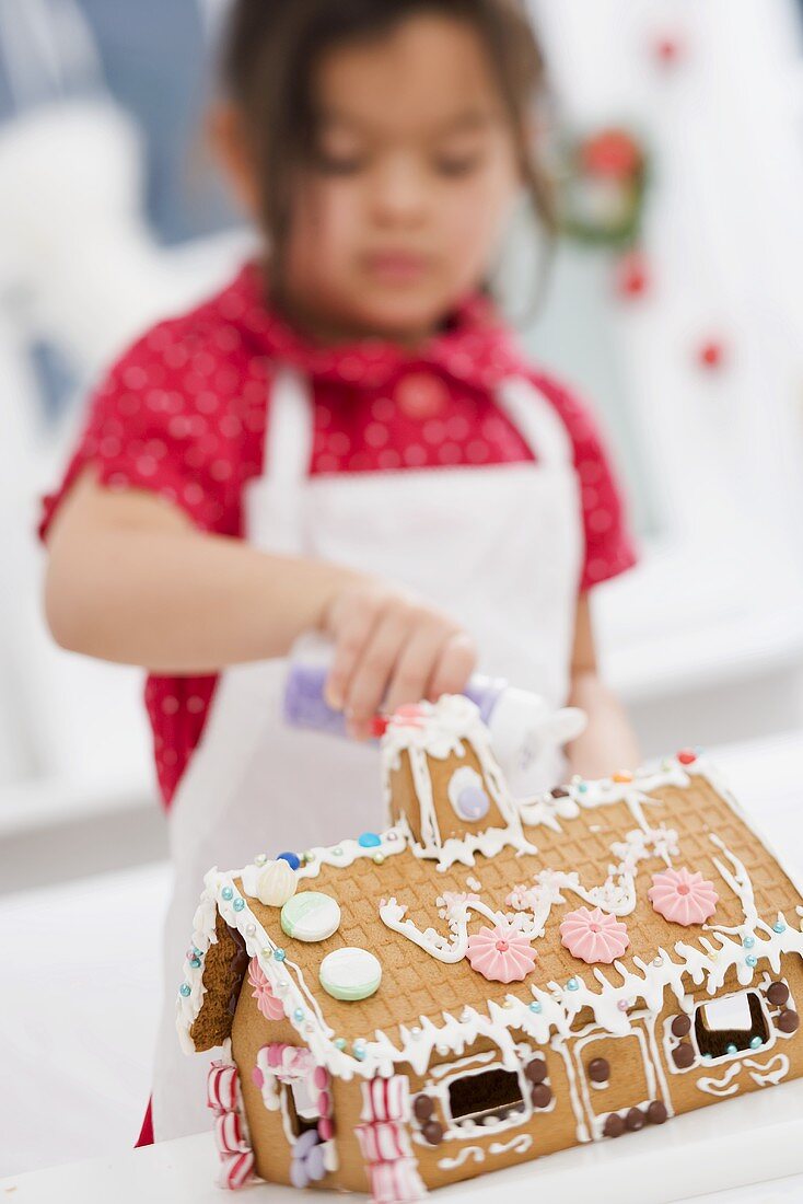 Kleines Mädchen verziert Lebkuchenhaus mit Zucker
