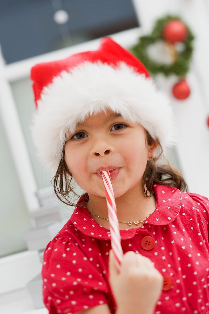 Kleines Mädchen mit Nikolausmütze isst Zuckerstange