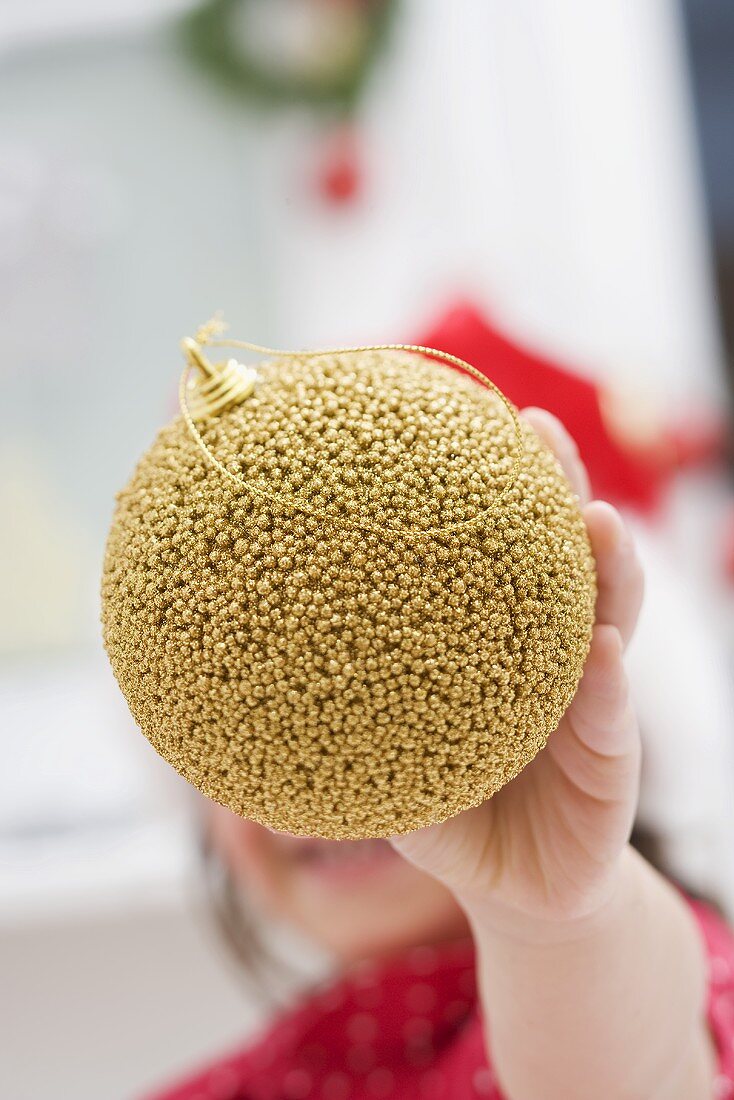 Kleines Mädchen mit Nikolausmütze hält Christbaumkugel