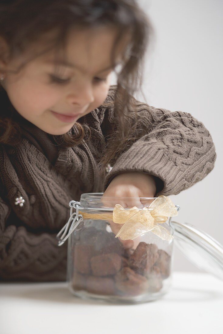 Girl reaching for chocolate biscuits in storage jar