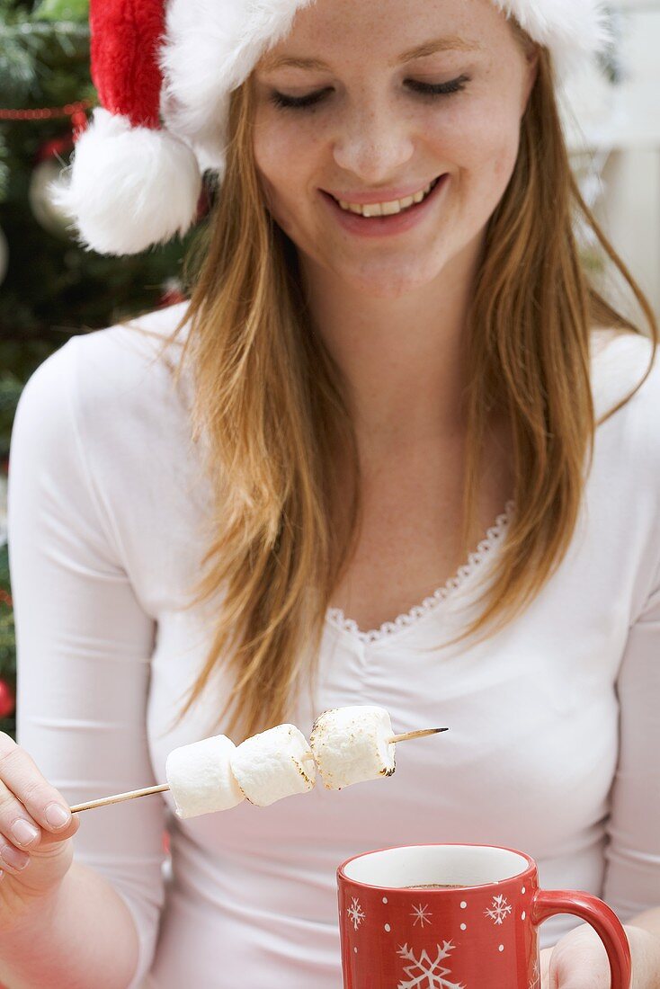 Frau mit Nikolausmütze hält Marshmallows und Tasse Kakao