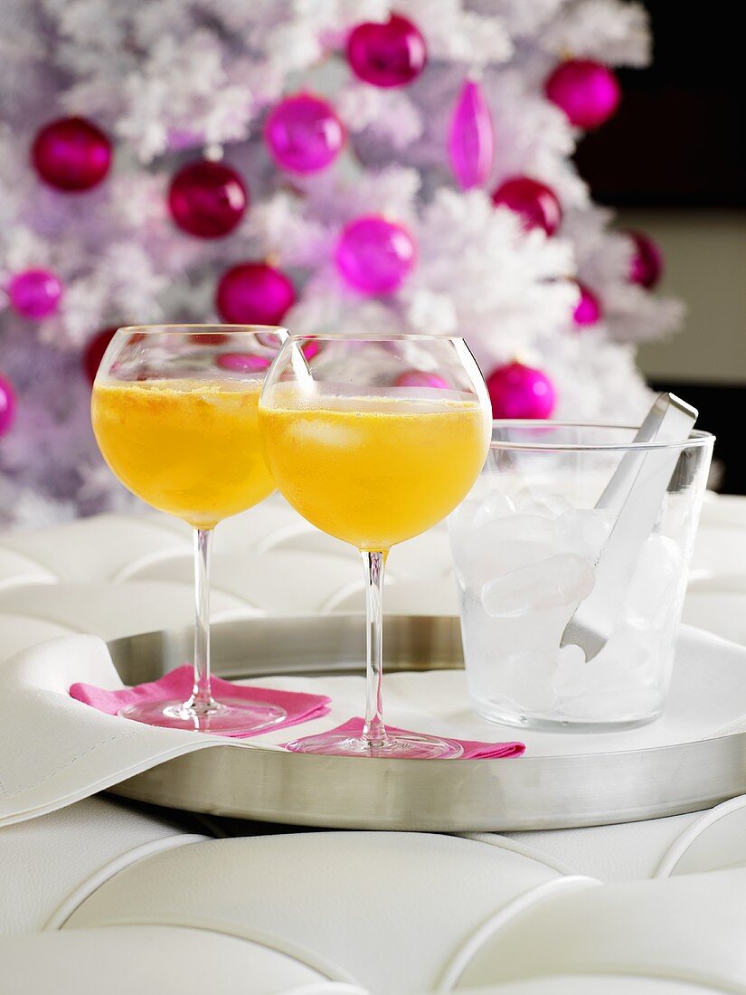 Orange drinks with ice cubes, Christmas tree in background
