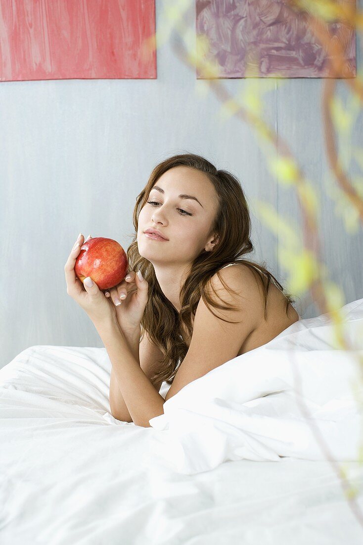 Junge Frau mit einem roten Apfel im Bett