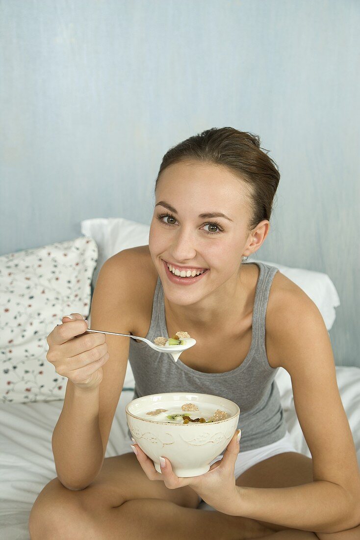 Junge Frau isst Müsli mit Joghurt im Bett