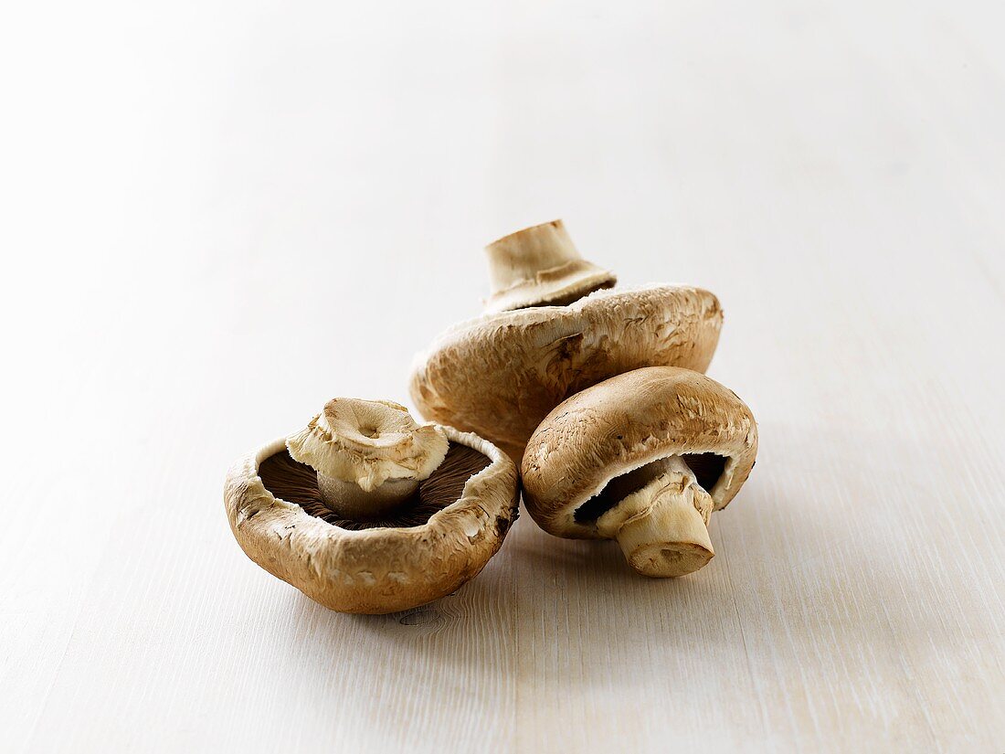 Three brown button mushrooms on white wooden table