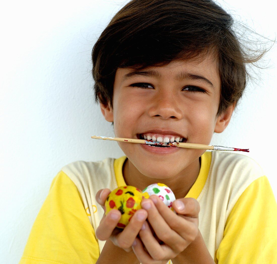 Boy with paintbrush in his mouth holding Easter eggs in his hands