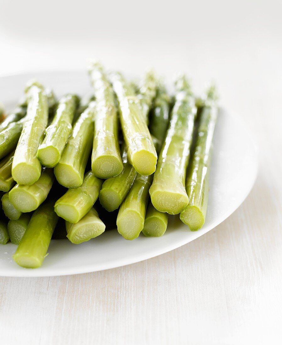 Cooked green asparagus spears on white plate