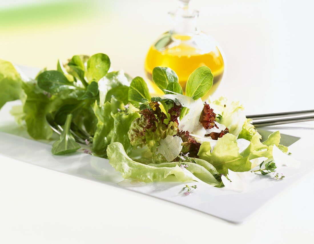 Mixed salad with Parmesan, bottle of oil in background