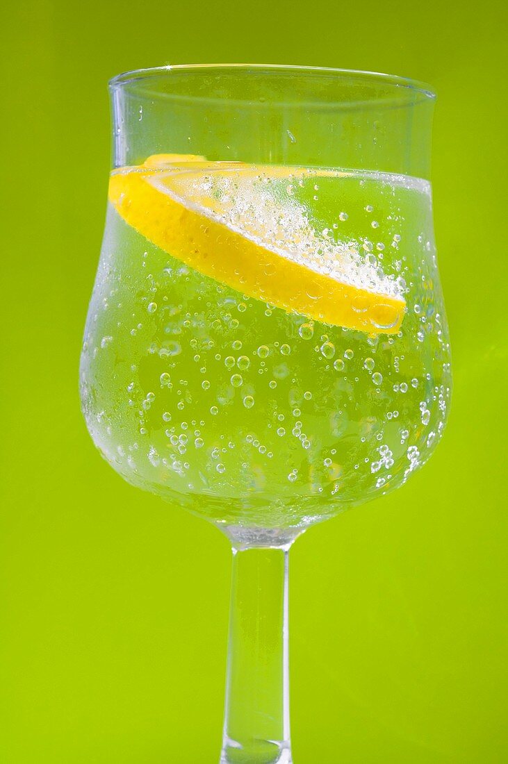 Ein Glas Wasser mit Zitronenscheibe vor grünem Hintergrund