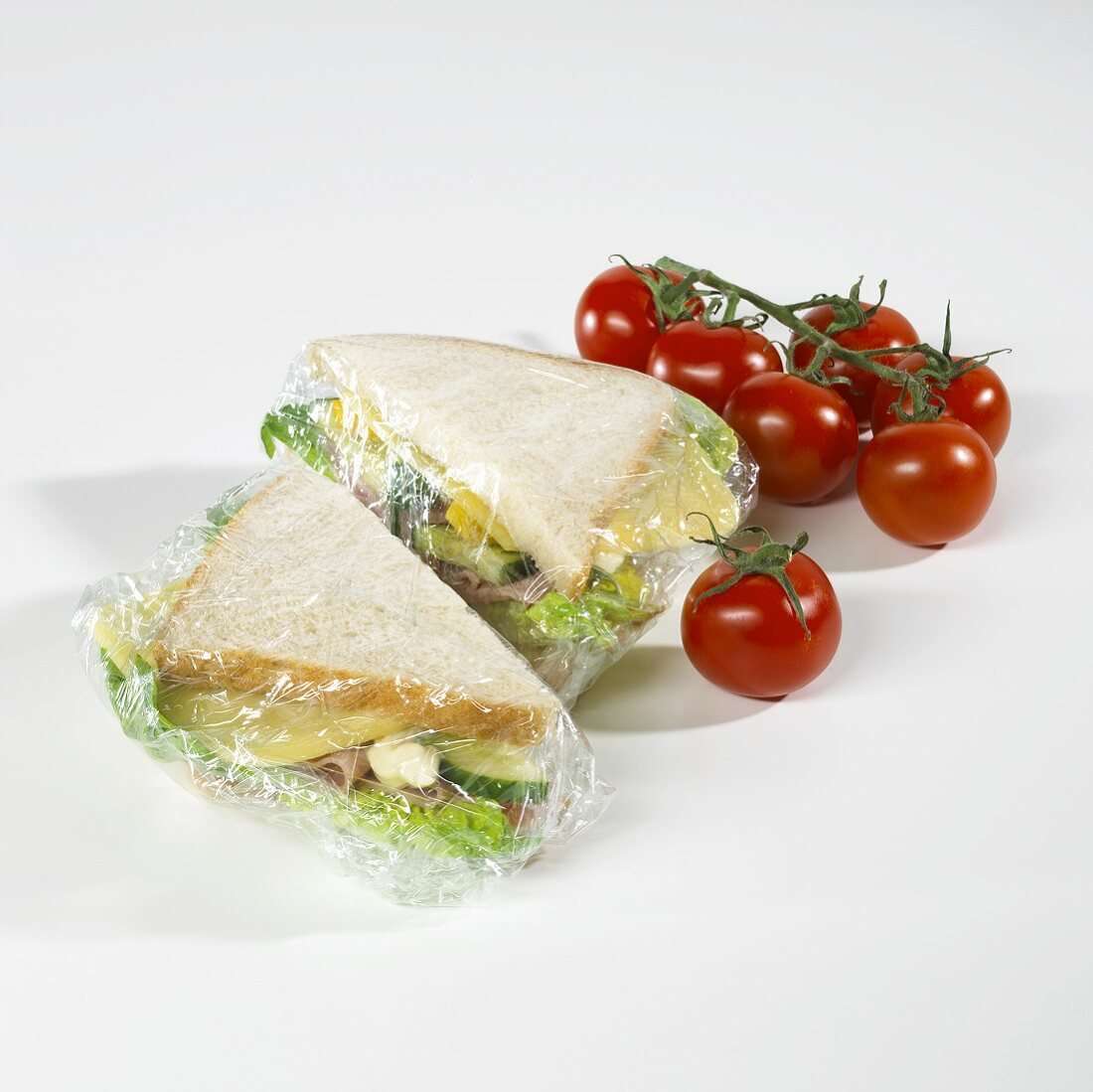 Sandwiches in clingfilm, tomatoes beside them