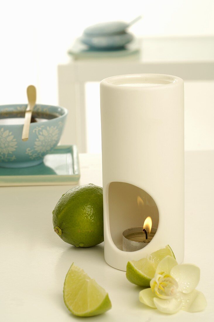 Scented lamp with limes, orchid flower and bowl of tea