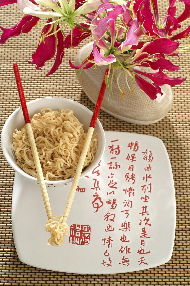 Bowl of Asian noodles with chopsticks and flowers