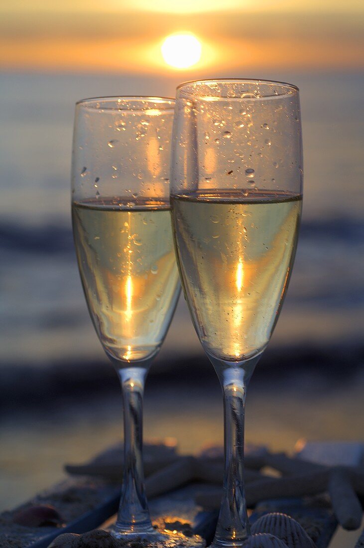 Two glasses of sparkling wine by the sea with setting sun