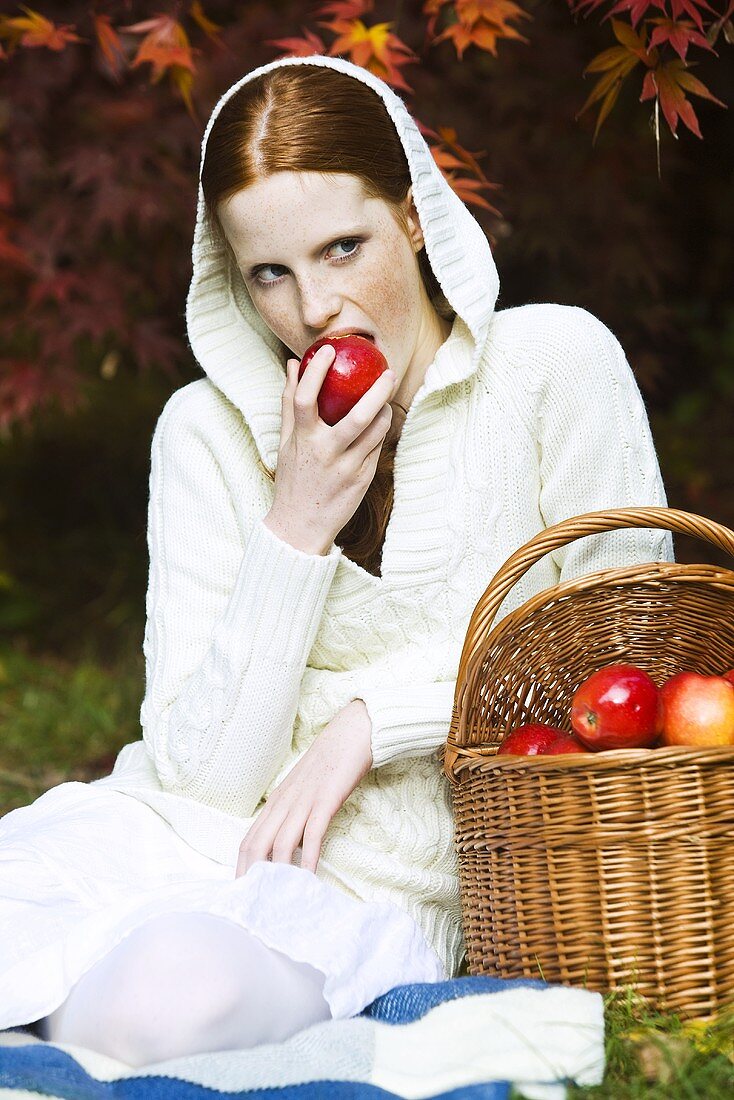 Young woman eating apple in park in autumn