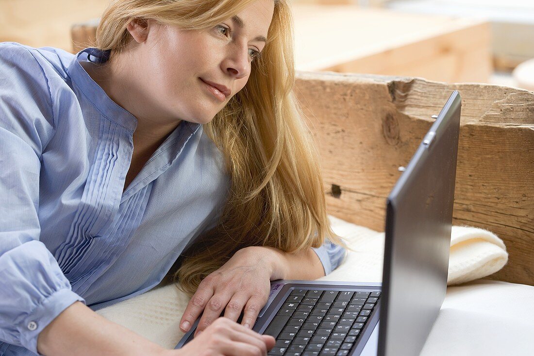 Blonde Frau mit Laptop auf dem Bett