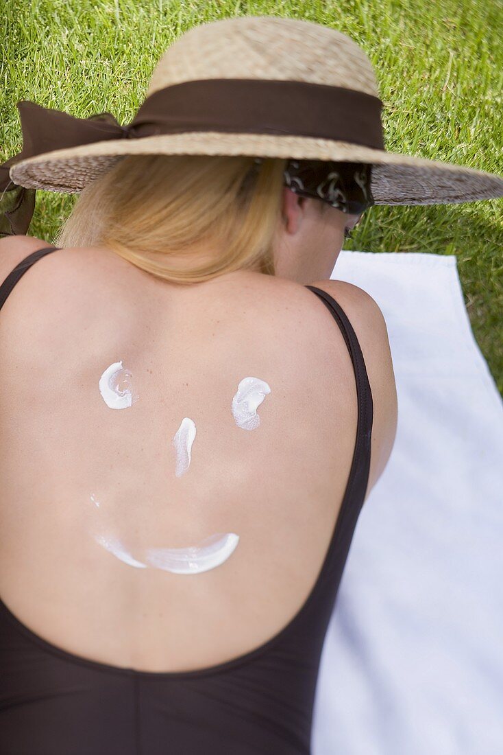 Frau mit Sonnenhut und Sonnencreme auf dem Rücken