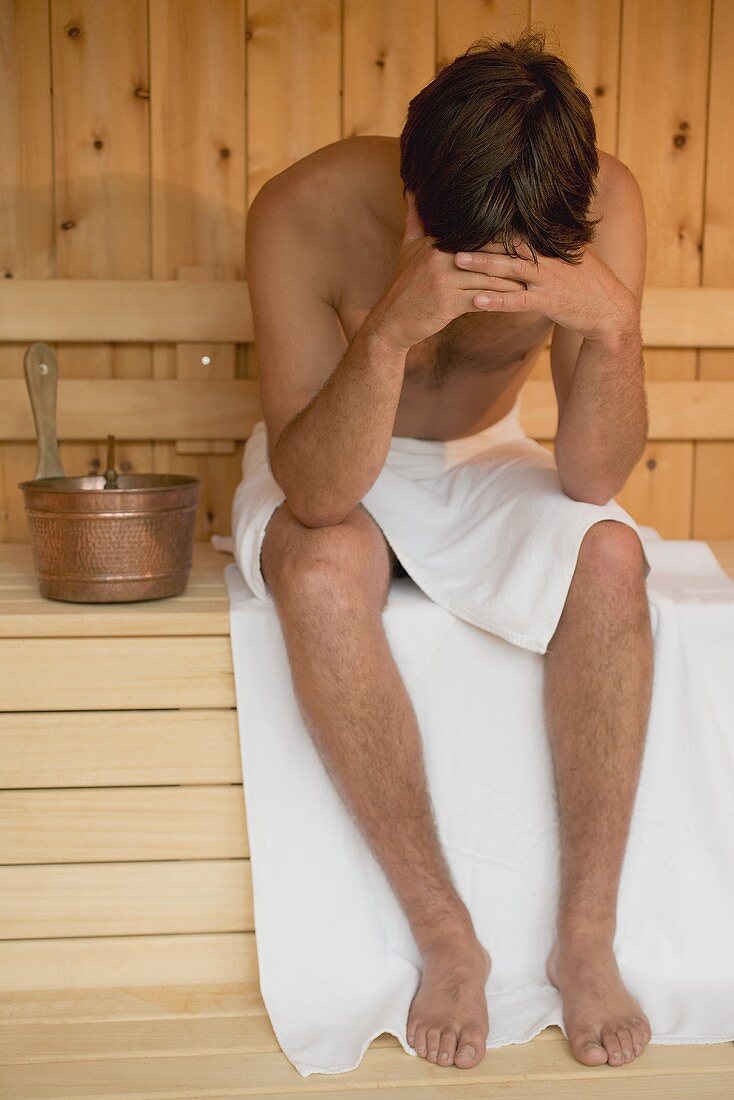 Mann sitzt in der Sauna neben Aufgusskübel