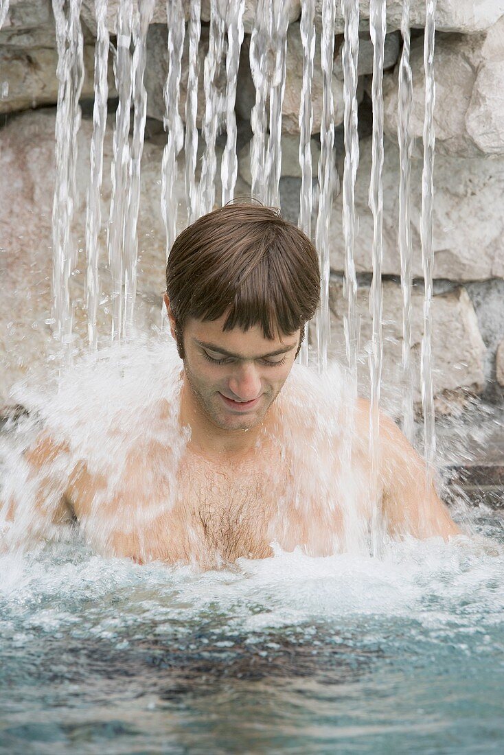 Young man standing under a waterfall