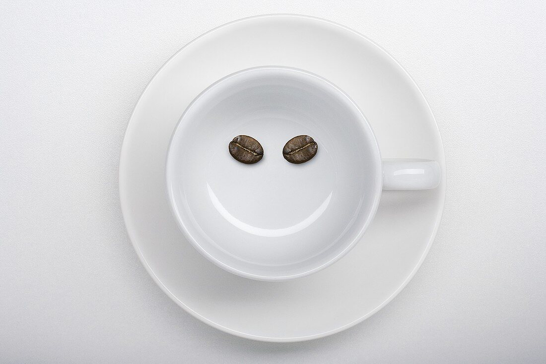 Eine Kaffeetasse mit zwei Kaffeebohnen als lächelndes Gesicht