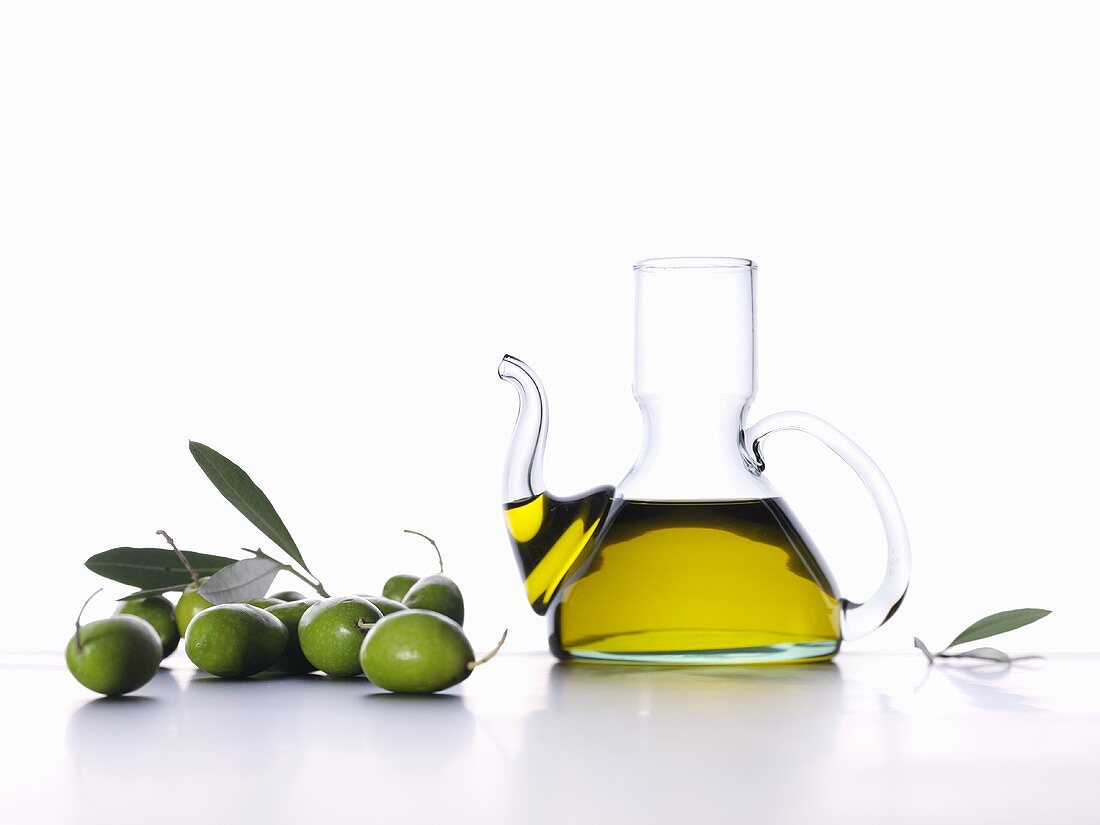 Olive oil in carafe, green olives and olive leaves