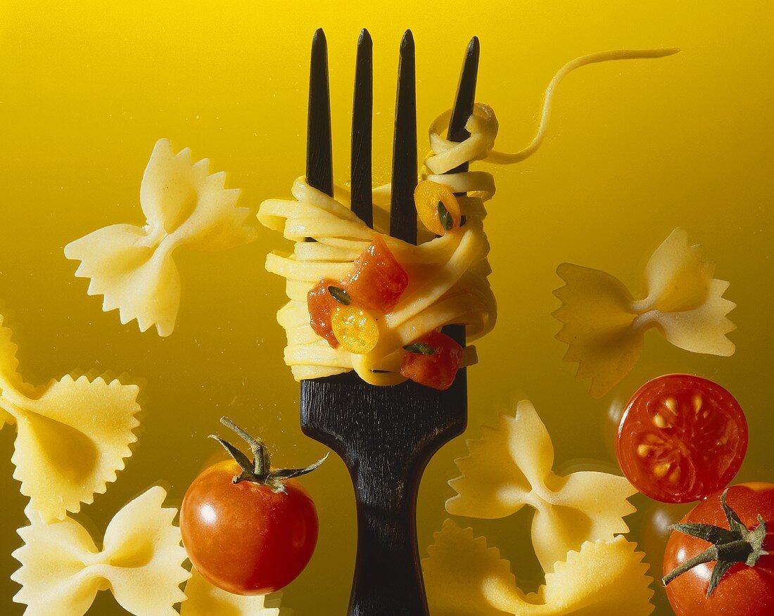 Dünne Bandnudeln mit Tomaten auf Gabel, daneben Farfallen