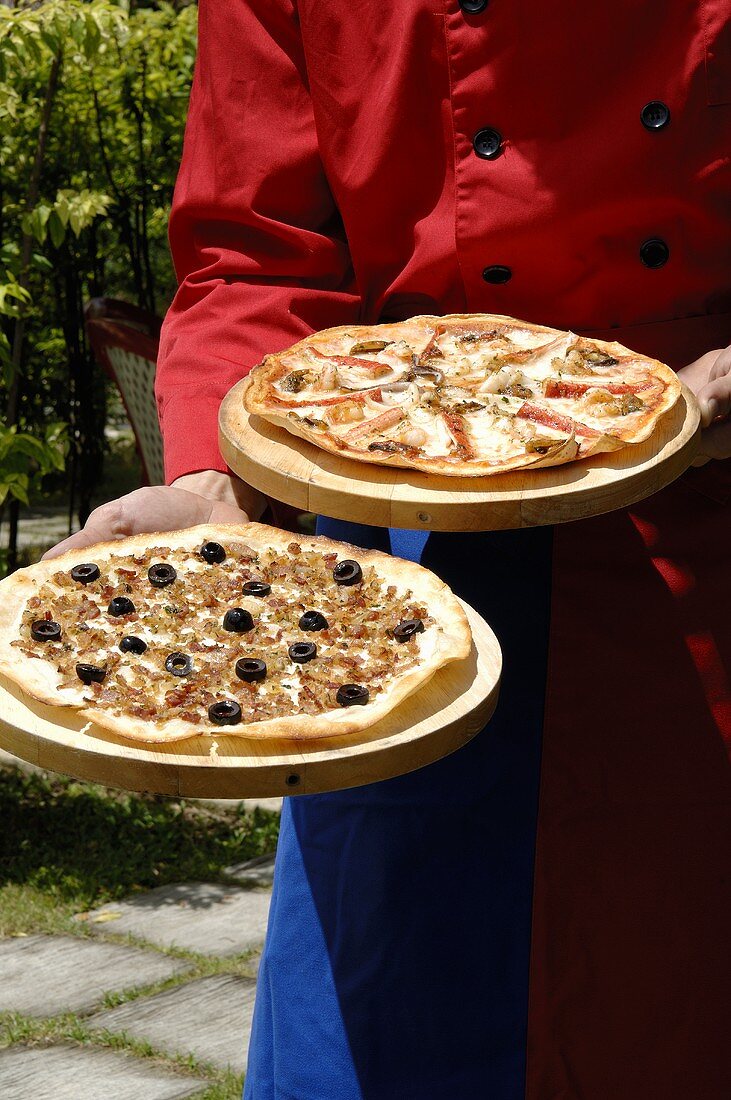 Koch trägt zwei Pizzen auf Holzbrettern