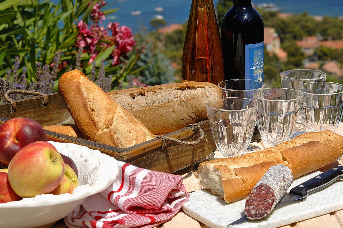 Baguette, salami, fruit and wine on laid garden table
