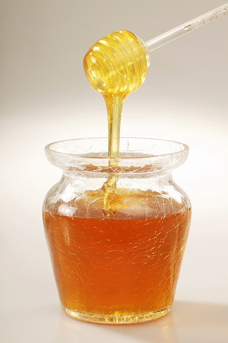 Honig tropft vom Acryllöffel ins Glas
