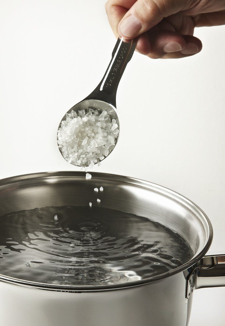 Einen Löffel Salz in einen Topf mit Wasser streuen