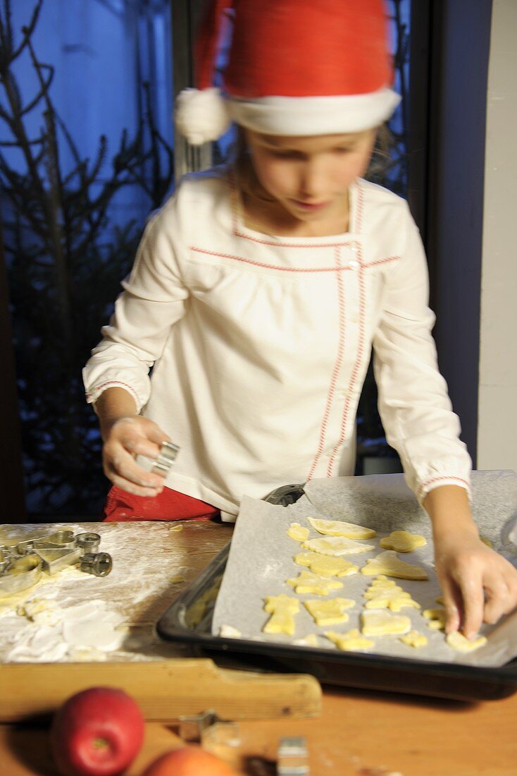 Mädchen legt ausgestochene Plätzchen auf Backblech