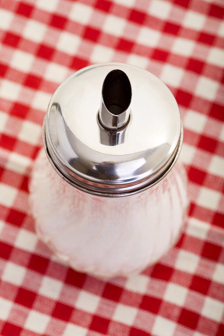 A sugar pourer on a checked table cloth