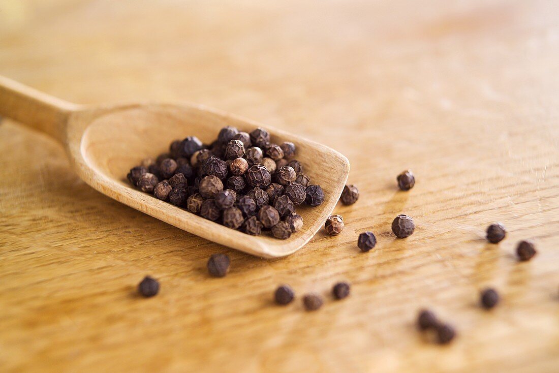 Black peppercorns on a wooden scoop