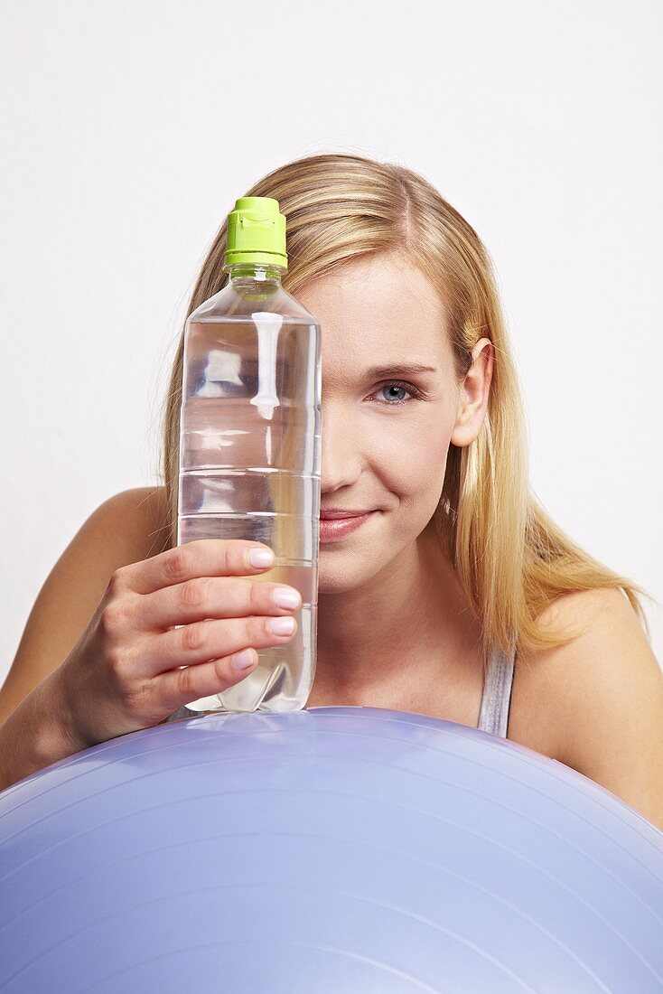 A young woman with a gym ball and a bottle of mineral water