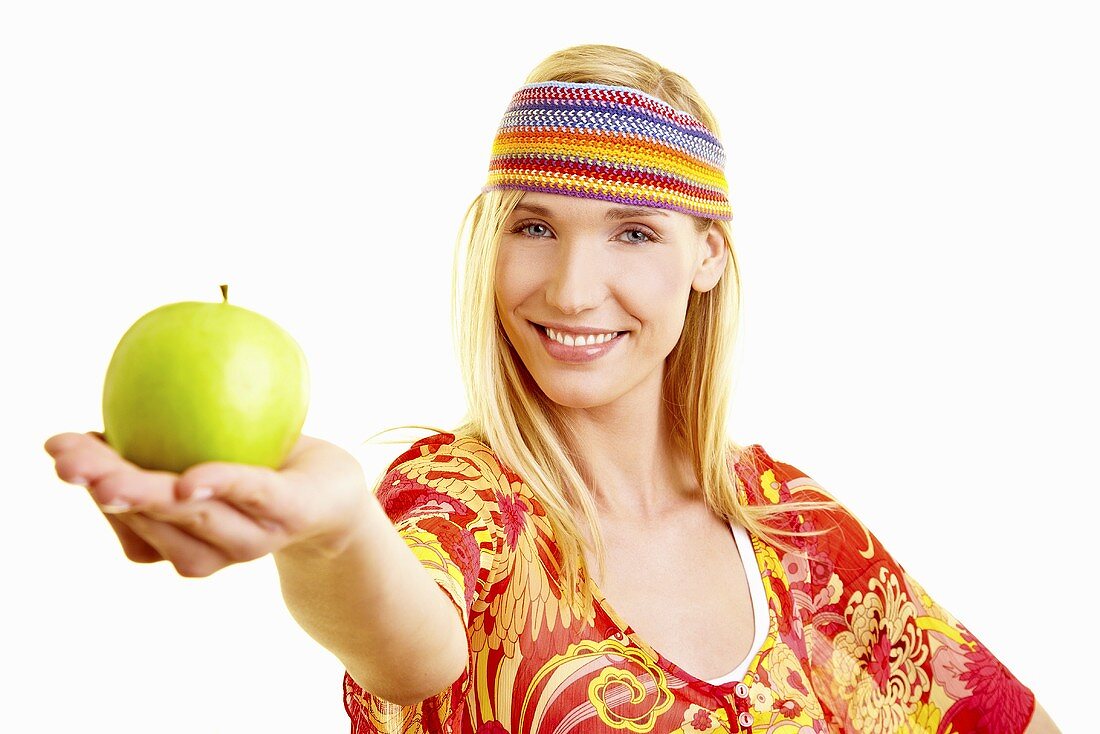 A young woman with a headband holding out a green apple