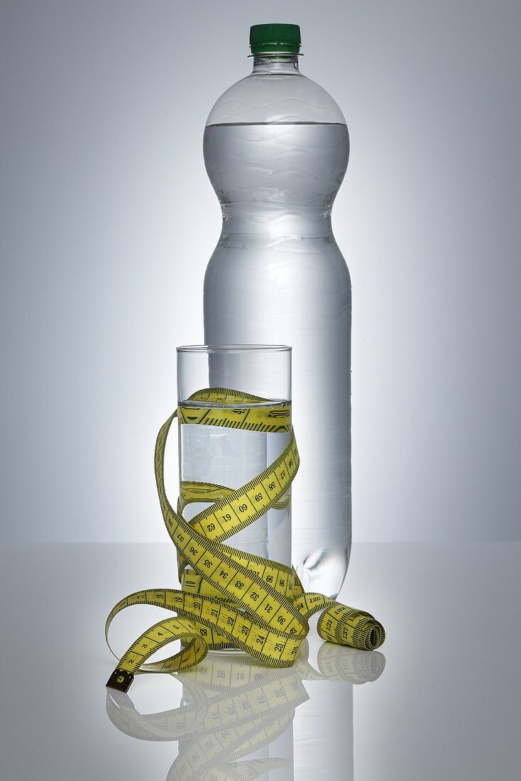 Wasserglas mit Massband vor Wasserflasche