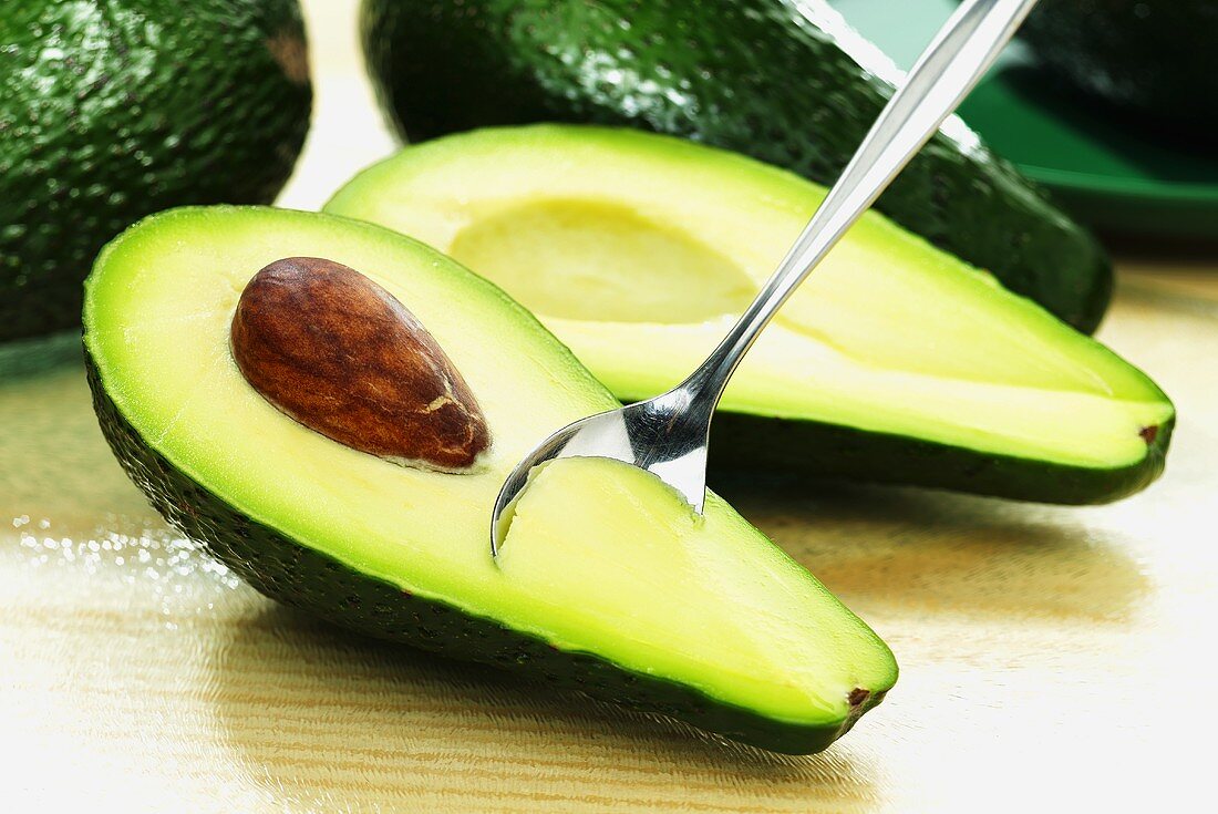 An avocado, halved, with a spoon