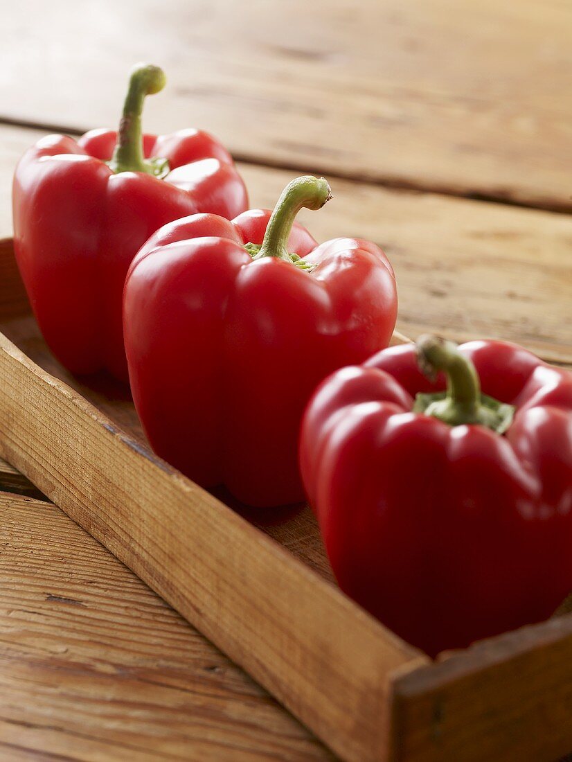 Three Fresh Red Bell Peppers in a Wooden Box