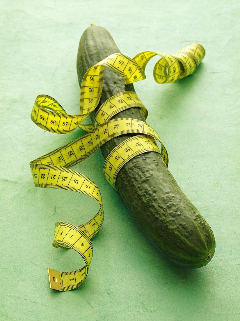 A cucumber with tape measure on a green surface