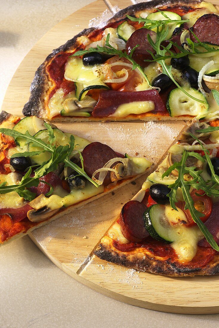 Salami and vegetable pizza with fresh rocket, a piece cut