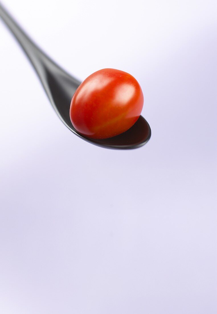 Red cocktail tomato on a black plastic spoon